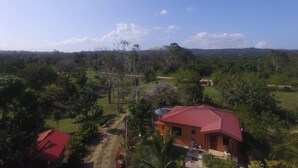 A rural house with a red roof, surrounded by lush greenery and a clear sky. - Aliana's Villas - Private Farm Home on the River (Gold Standard Certified) (San Ignacio)