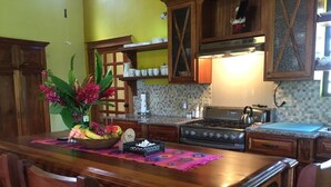 A kitchen with wooden cabinets, a central island, and a dining area with chairs. - Aliana's Villas - Private Farm Home on the River (Gold Standard Certified) (San Ignacio)