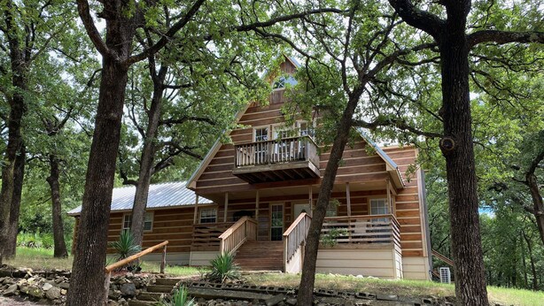 A log cabin with a balcony, surrounded by trees. - Beautiful Longhorn Lodge at Lake Texoma! (Gordonville)