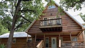A wooden cabin with a balcony, a front door, and a staircase leading to the entrance. - Beautiful Longhorn Lodge at Lake Texoma! (Gordonville)