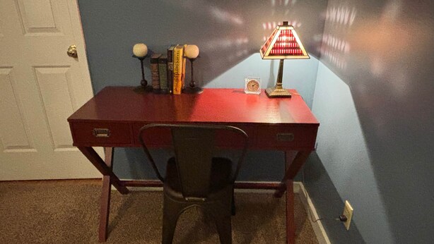 Uma mesa vermelha com uma cadeira, uma lâmpada e alguns livros.
