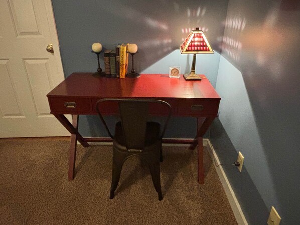 Un escritorio rojo con una silla, una lámpara y algunos libros.