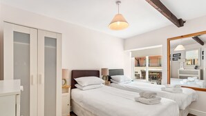 A hotel room with two beds, a wardrobe, a mirror, and a view of a traditional sweet shop. - Kilmore - Direct Beach Access, Sea Views (Saundersfoot)
