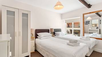 A hotel room with two beds, a wardrobe, a mirror, and a view of a traditional sweet shop.