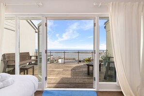 Una stanza con un letto, una panca in legno e vista sulla spiaggia tramite una porta di vetro.