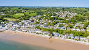 An aerial view of a coastal town with a beach house labeled, featuring a mix of residential buildings, green fields, and a sandy beach. - Kilmore - Direct Beach Access, Sea Views (Saundersfoot)