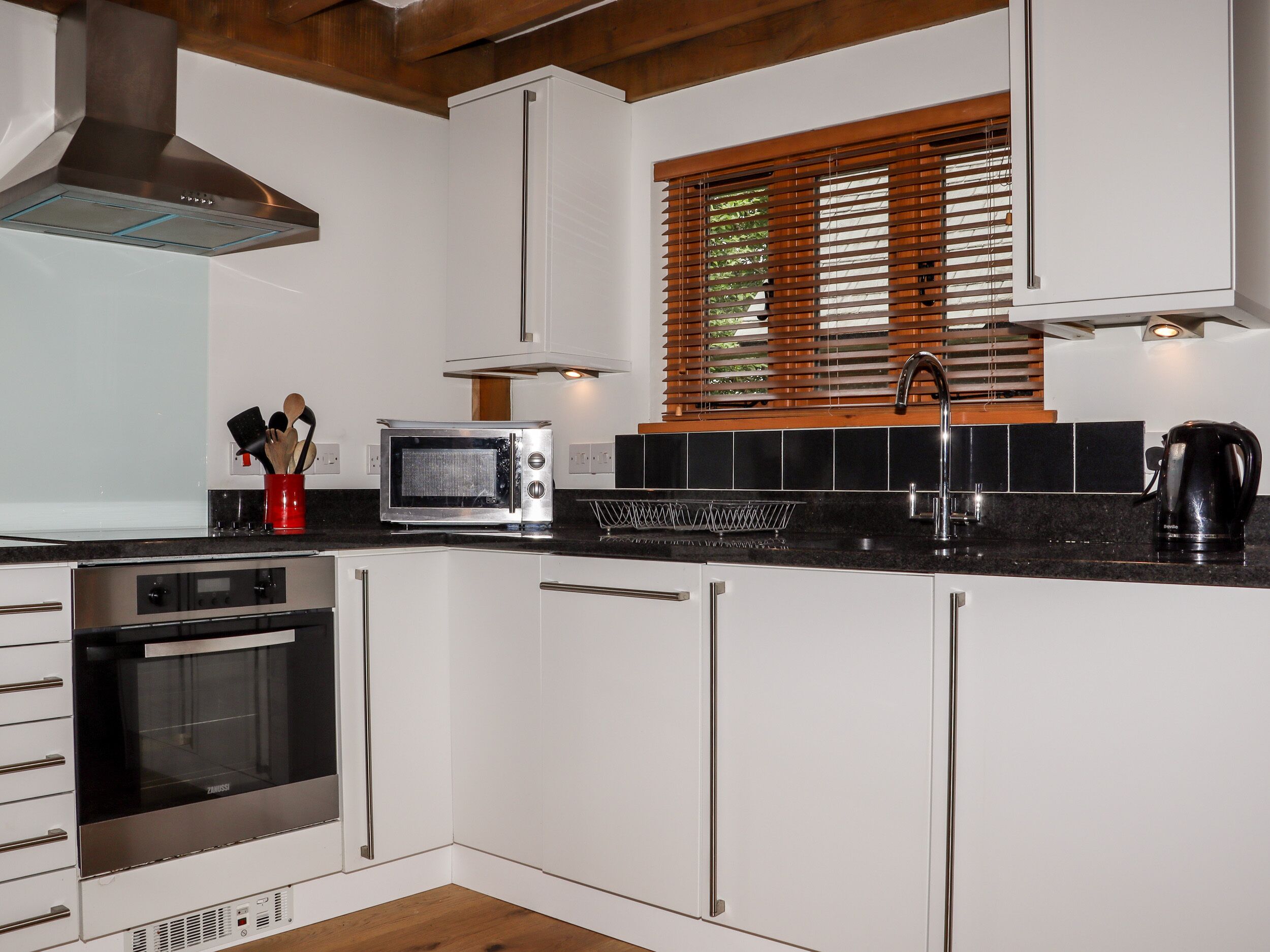A modern kitchen with white cabinets, a built-in oven, a microwave, and a coffee maker.
