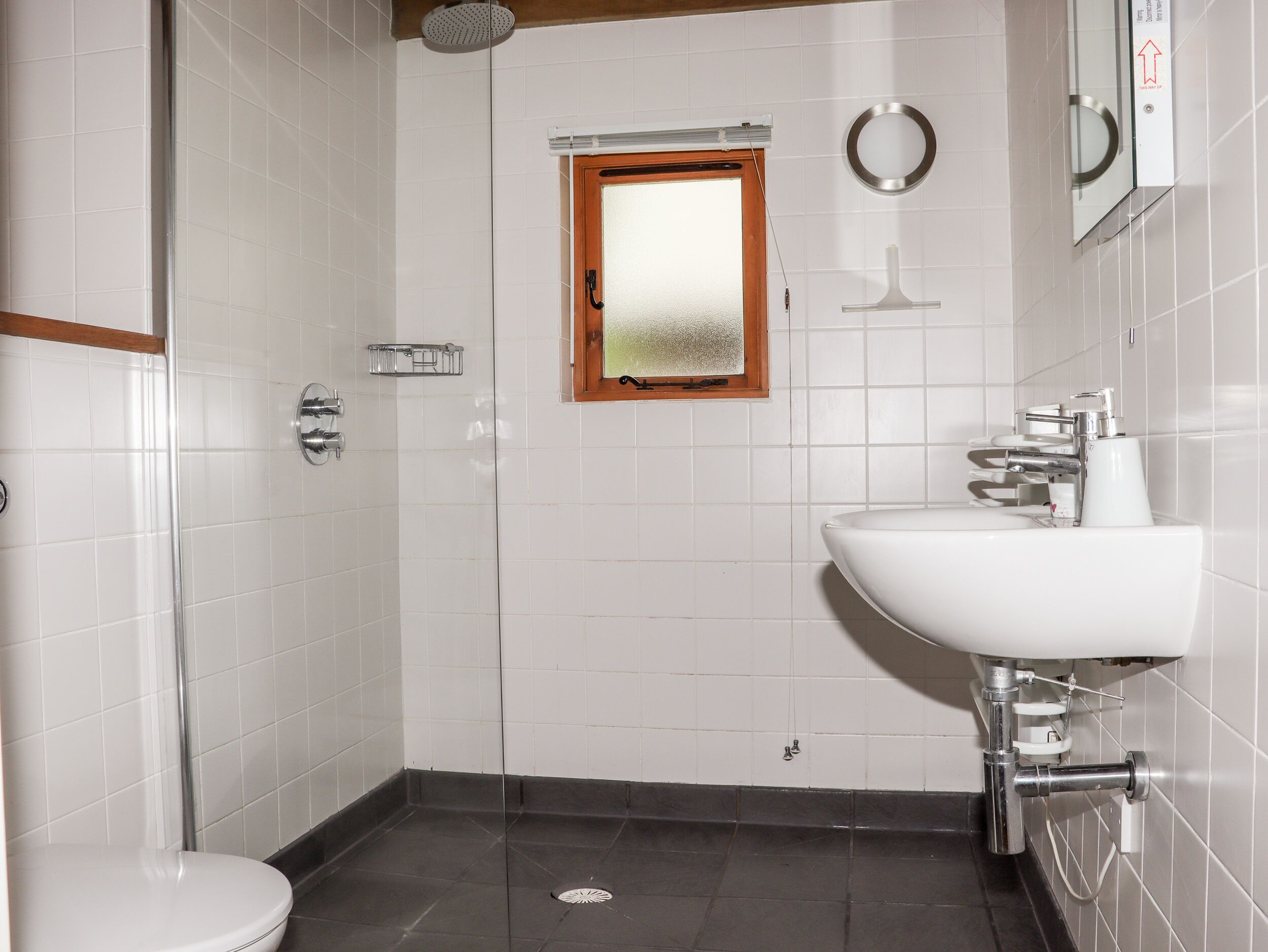 Un baño con lavamanos blanco, un espejo y ducha.