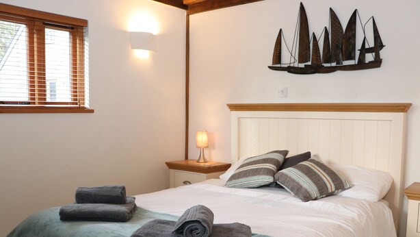 Ein ordentlich bezogenes Bett mit einem türkisfarbenen Bettüberwurf und zwei Kissen, einer Nachttischlampe sowie einer an der Wand befestigten Segelboot-Dekoration.