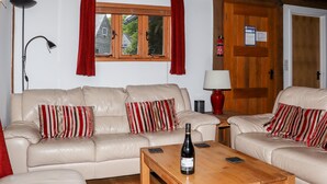 Ein gemütliches Wohnzimmer mit zwei beigen Ledersofas, roten und weißen Streifen-Kissen, einem Holztisch mit einer Weinflasche, einer roten Stehlampe und einem Fenster mit roten Vorhängen.