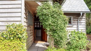 Ein Holzhaus mit überdachter Veranda, sichtbarer Küchenzeile und einem Garten mit verschiedenen Pflanzen.