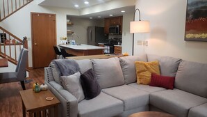 A spacious living room with a grey sectional sofa, a wooden coffee table, and a wooden side table with decorative pumpkins. A staircase with wooden railings leads to an upper level. - Perfect Getaway - Cozy Cottage in The Galena Territory (Galena)