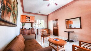 A living room with a sofa, chairs, a small round table, wooden cabinets, a painting, and a window.
