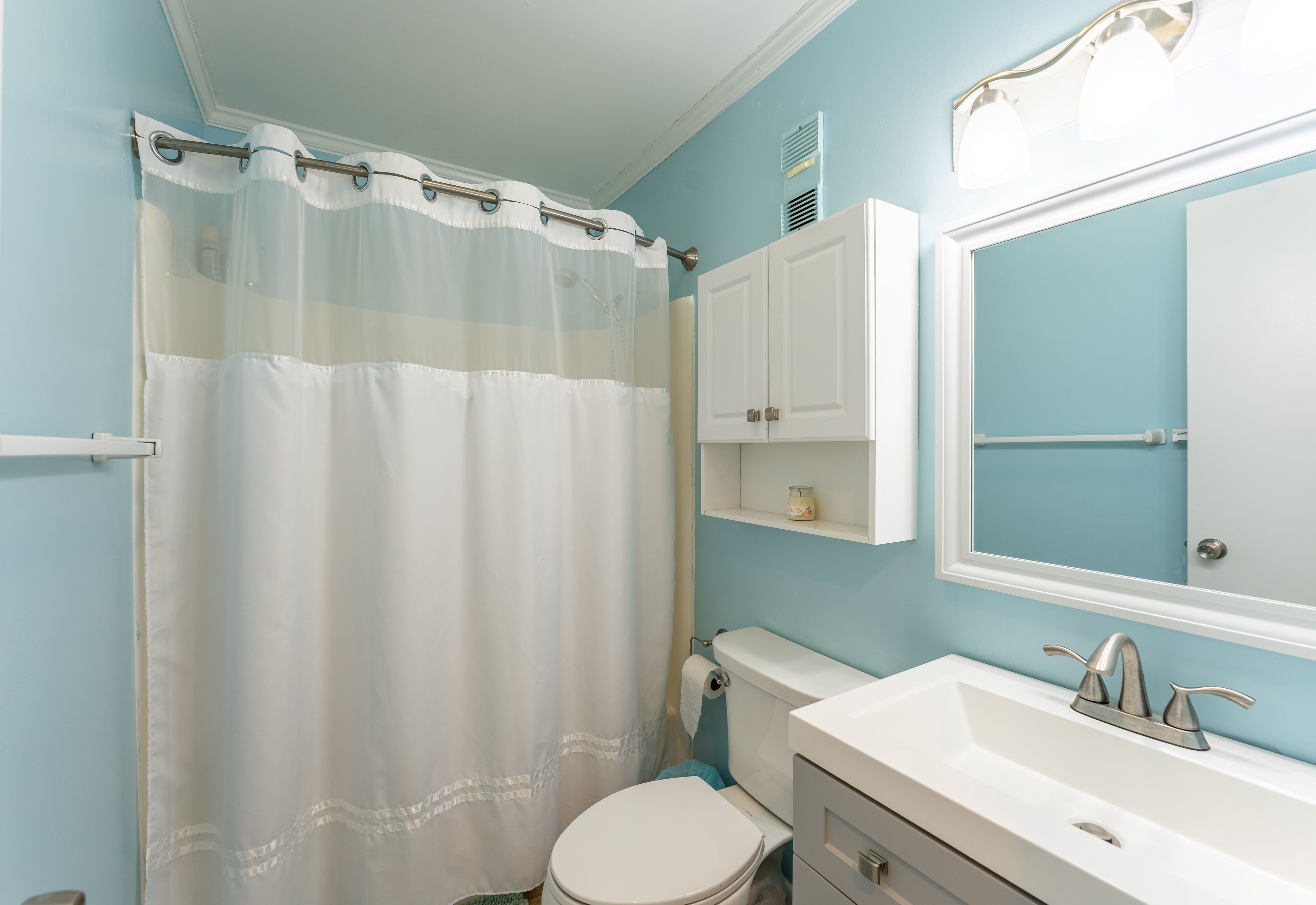 A bathroom with a shower curtain, toilet, sink, and mirror.