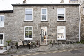 A stone building with a front door, a bench, and potted plants.