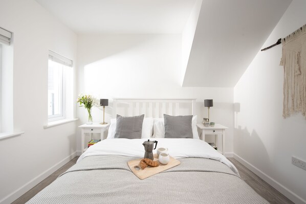 A neatly arranged bedroom with a bed, bedside tables, a nightstand, a window, and a wall-mounted macrame piece.