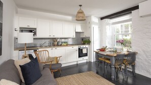 Una cocina moderna con armarios blancos, un comedor con mesa y sillas, y un amplio ventanal que proporciona luz natural.