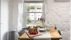 Un comedor con una mesa de madera preparada para dos personas, mostrando pan, tomates y un jarrón con flores.