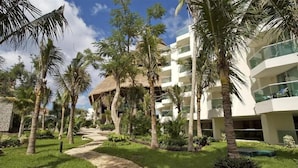 A resort with a pathway, palm trees, and a modern building with balconies. - Cozumel Spacious Studio with Beach & Pools (San Miguel de Cozumel)