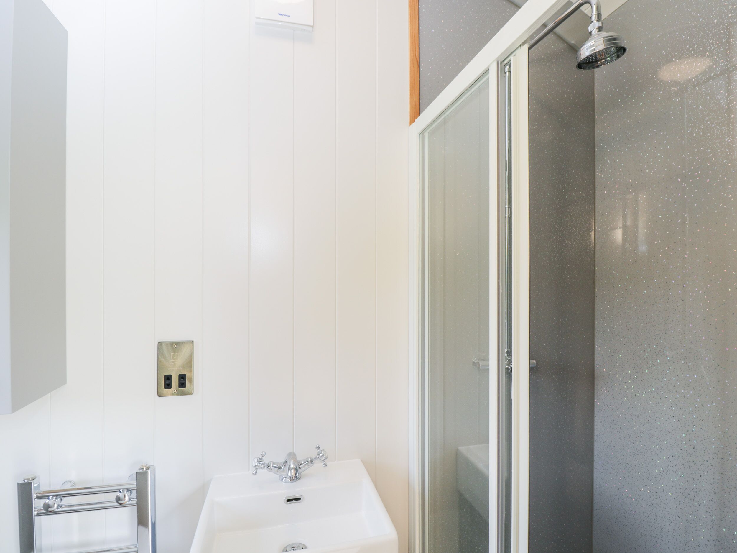 A bathroom with a white sink, a shower with a glass door, and a towel rack.
