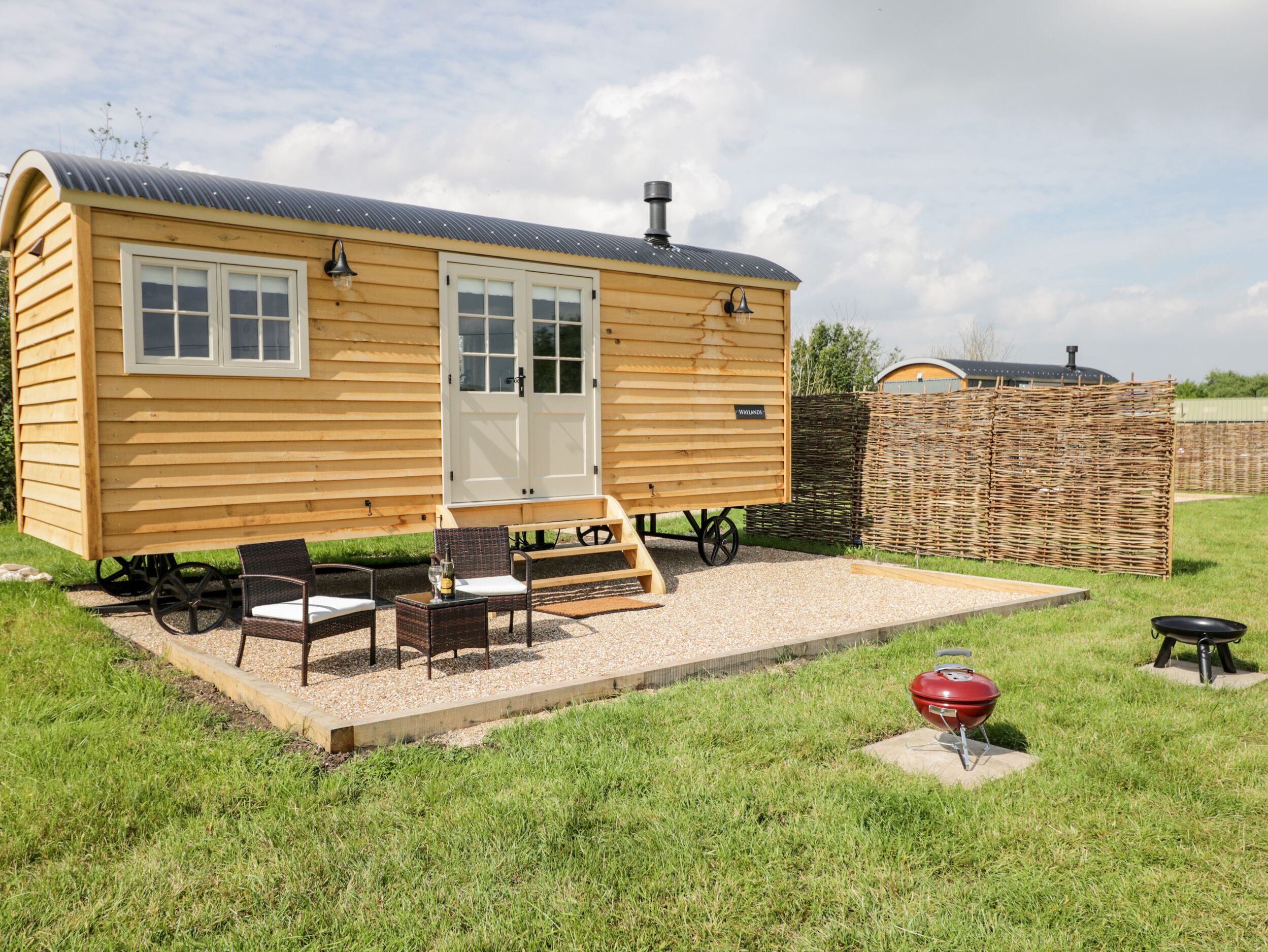 A wooden cabin with a porch, two chairs, a table, and a barbecue grill.