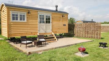 A wooden cabin with a porch, two chairs, a table, and a barbecue grill.