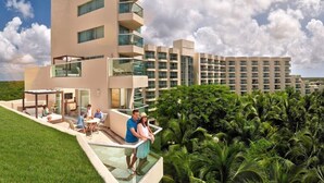 A modern hotel with a glass exterior, a rooftop patio, and lush greenery. - Beach-front Studio with Balcony for Weekend Getaway (San Miguel de Cozumel)