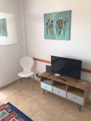 A living room with a white chair, a TV on a wooden stand, and a painting on the wall.