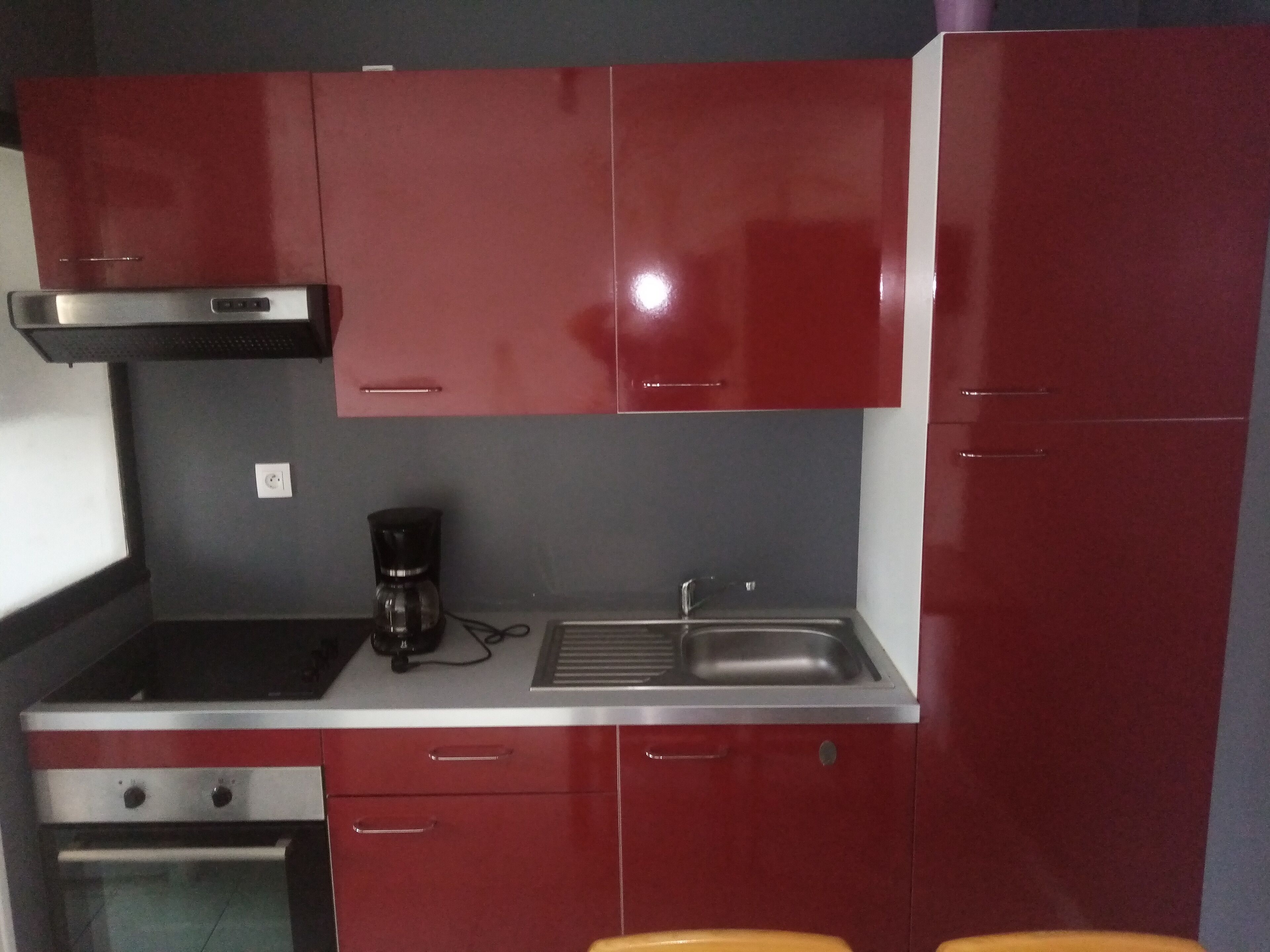 Una cuina compacta amb armaris vermells, un fogó d'acer inoxidable, una cafetera i un rentaplat.