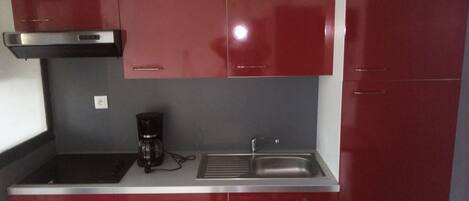 Una cuina compacta amb armaris vermells, un fogó d'acer inoxidable, una cafetera i un rentaplat.