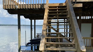 Un muelle de madera con una escalera que lleva a una terraza, con vista a una masa de agua tranquila.