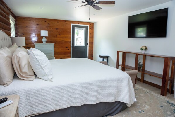 A bedroom with a large bed, wooden walls, a ceiling fan, a TV, and a dresser.