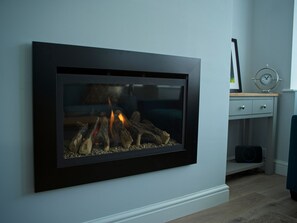 A modern fireplace with a glass front, set against a light-colored wall. - Sam's Place (Whitby)