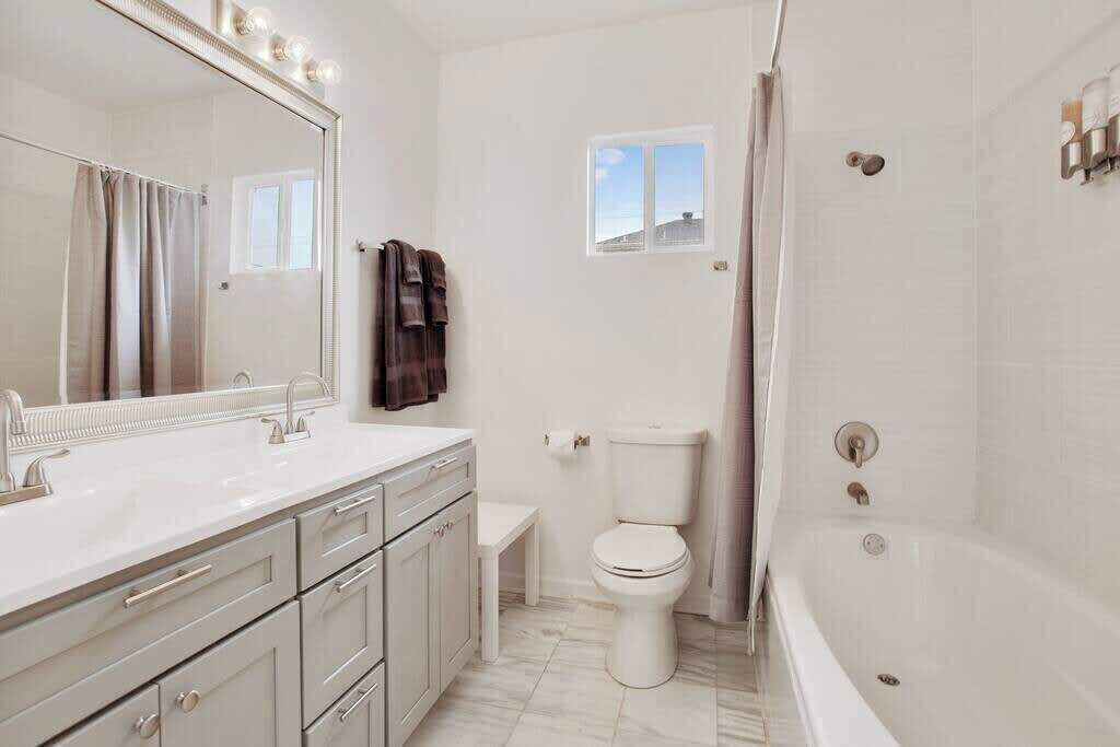 Un bagno moderno con uno specchio grande, sanitari bianchi, una vasca e un water.