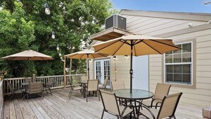 Una terraza de madera con mobiliario exterior y sombrillas, una puerta y una unidad de aire acondicionado en la casa.