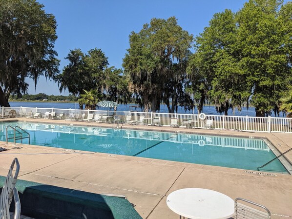 A swimming pool with lounge chairs and umbrellas, surrounded by trees and a view of a lake.