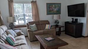 Una sala de estar con un sofá color crema, una mesa de centro, un televisor y un cuadro en la pared.