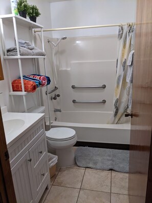 A bathroom with a white bathtub, a toilet, a sink, and a shelf with towels and a potted plant. - Lake front cottage (Salt Springs)