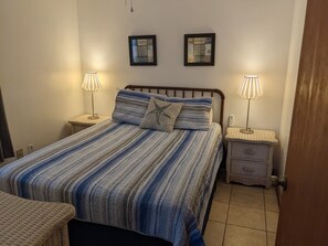 A bedroom with a bed, two nightstands, two wall-mounted lamps, and two framed pictures. - Lake front cottage (Salt Springs)