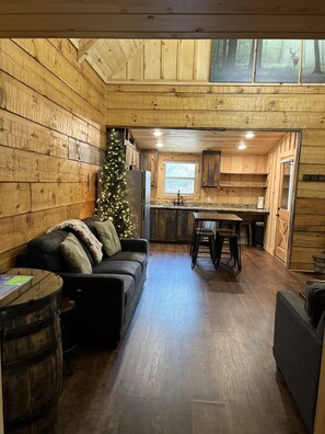 A cozy cabin interior with a wooden interior, a Christmas tree, a sofa, and a dining area.