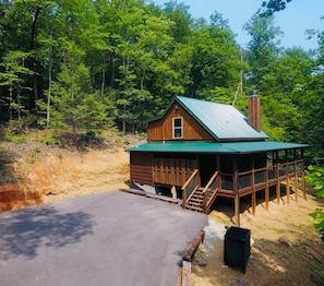 A wooden cabin with a green roof, a porch, and a staircase leading to a deck.