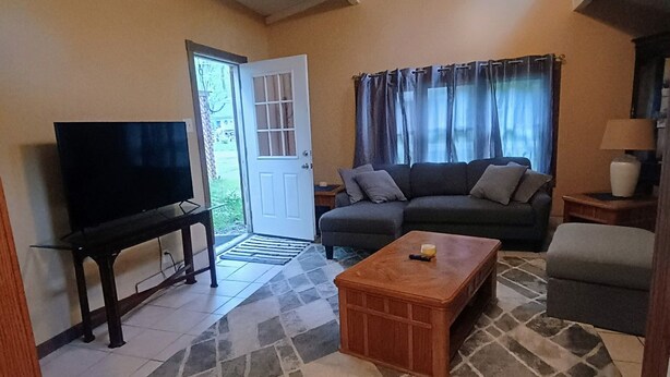 A living room with a television, sofa, coffee table, and a ceiling fan. - Cozy Cottage (Ashville)