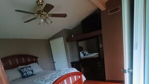 A bedroom with a wooden bed, a ceiling fan, a dresser, and a door leading to another room. - Cozy Cottage (Ashville)