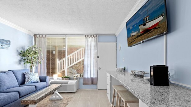 Een moderne woonkamer met een blauwe bank, een salontafel en een keuken met een marmeren aanrecht en barkrukken.