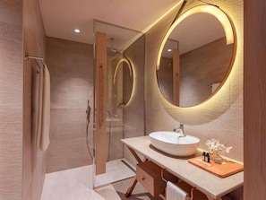 A modern bathroom with a glass shower enclosure, a vanity with a large mirror, and a sink with a wooden countertop.