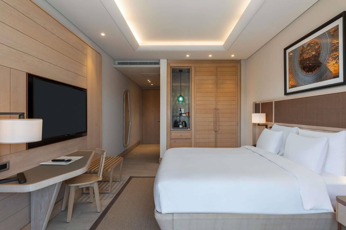 Una habitación de hotel moderna con una cama grande, un escritorio con una silla, un televisor y una obra de arte enmarcada en la pared.
