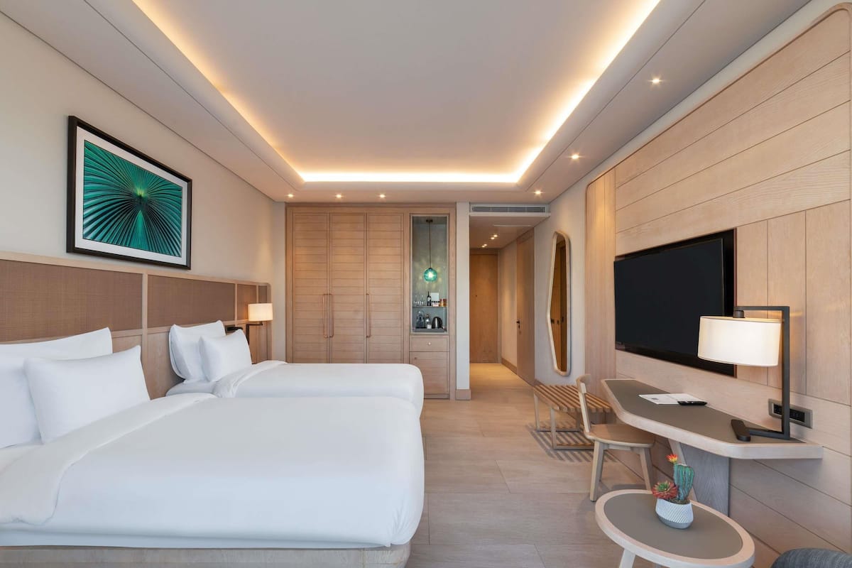 Habitación de hotel con una cama grande, un escritorio con televisor, un espejo y una mesita con una planta.