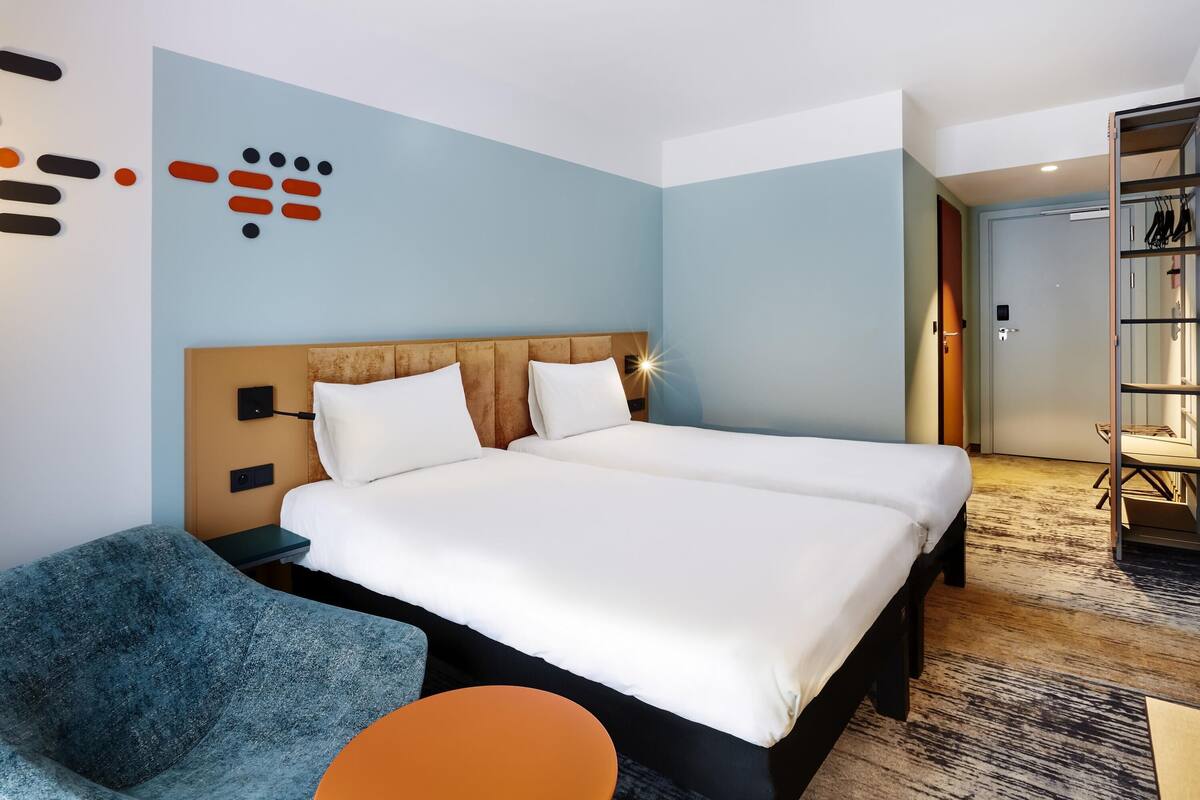 A hotel room with a bed, a chair, a small table, and a wardrobe.