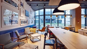 Una cafetería moderna con una larga mesa de madera, asientos cómodos y grandes ventanales que ofrecen vistas al exterior.