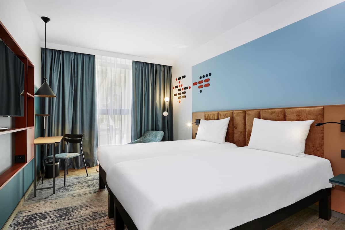 A hotel room with a large bed, a desk, a chair, and a TV.